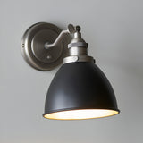 Endon Bramdale industrial wall light with adjustable knuckle, matt black dome shade and aged pewter fitting, mounted on a light grey wall.
