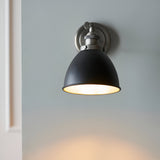 Endon Bramdale wall light with matt black dome shade and aged pewter adjustable knuckle, illuminated and mounted on a pale grey wall.
