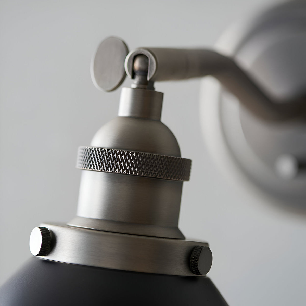 Close-up of the Endon Bramdale wall light's aged pewter knuckle joint, knurled socket collar and matt black shade with thumbscrew fittings.