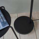Bramdale Floor Lamp in black, close-up of round matte base and metal pole on a wooden floor beside a black side table.