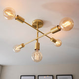 Endon Marlowe 5 light semi-flush ceiling light in satin brass, with crossed arms holding five E27 globe bulbs against a white ceiling.