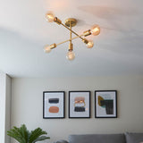 Endon Marlowe 5 Light Semi-Flush Ceiling Light in satin brass with exposed E27 bulbs on crossed arms, installed above a living room artwork display.