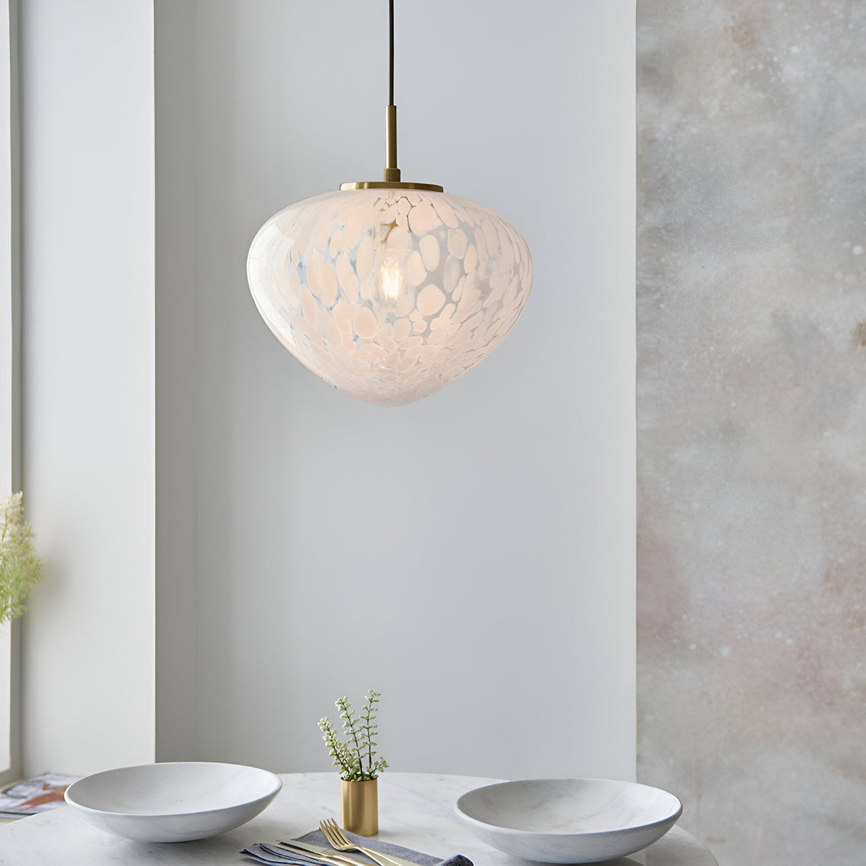 Calloway Pendant in Brass & White, a single-light fixture with a speckled confetti-effect glass shade on satin brass fittings, shown above a dining table.