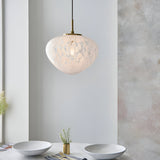Calloway Pendant in Brass & White, a single-light fixture with a speckled confetti-effect glass shade on satin brass fittings, shown above a dining table.