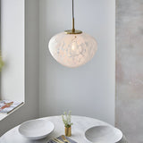 Calloway Pendant in brass and white, single-light fixture with speckled confetti glass shade, hung above a marble dining table.