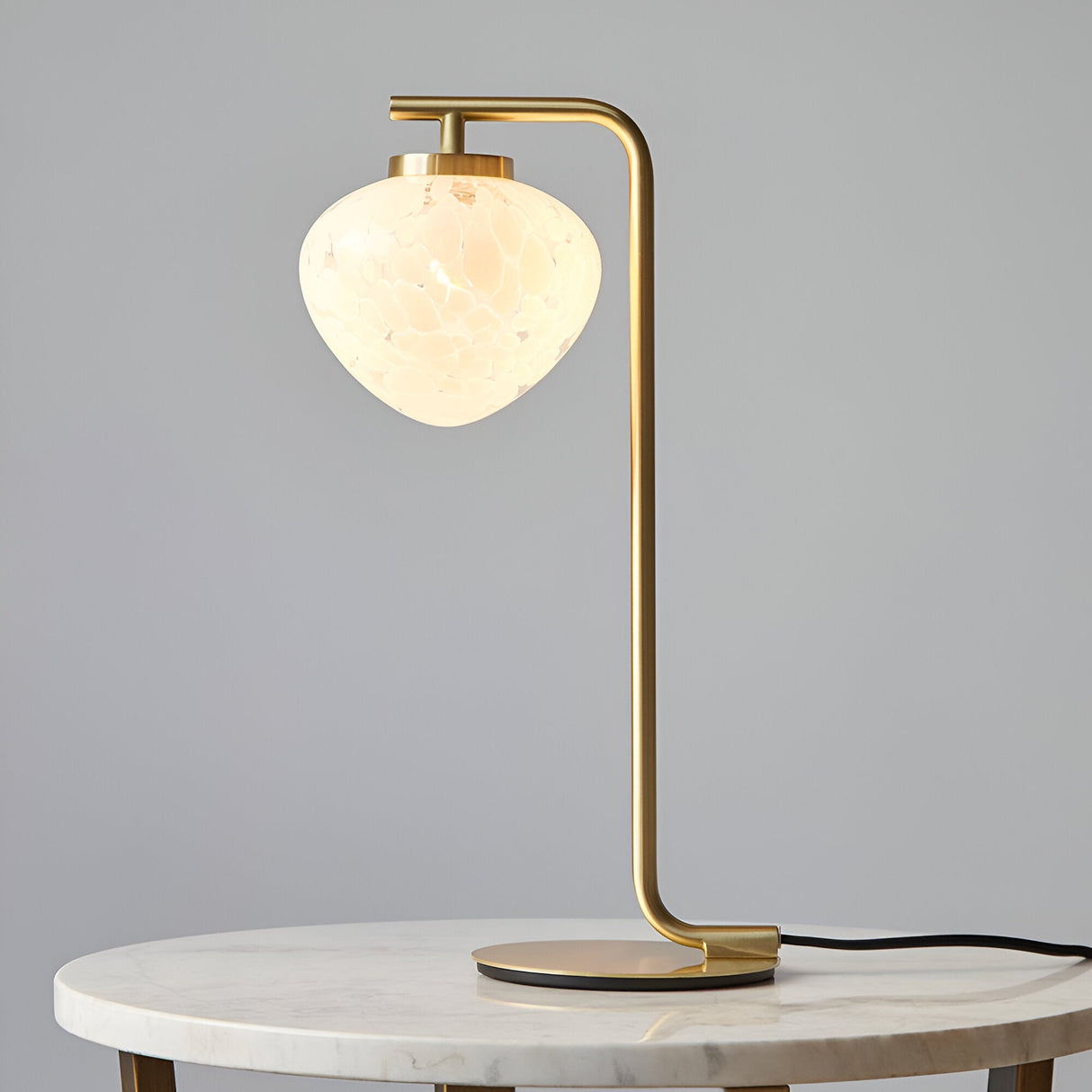 Endon Calloway table lamp in satin brass with a white confetti blown glass shade, shown on a round marble side table against a grey background.