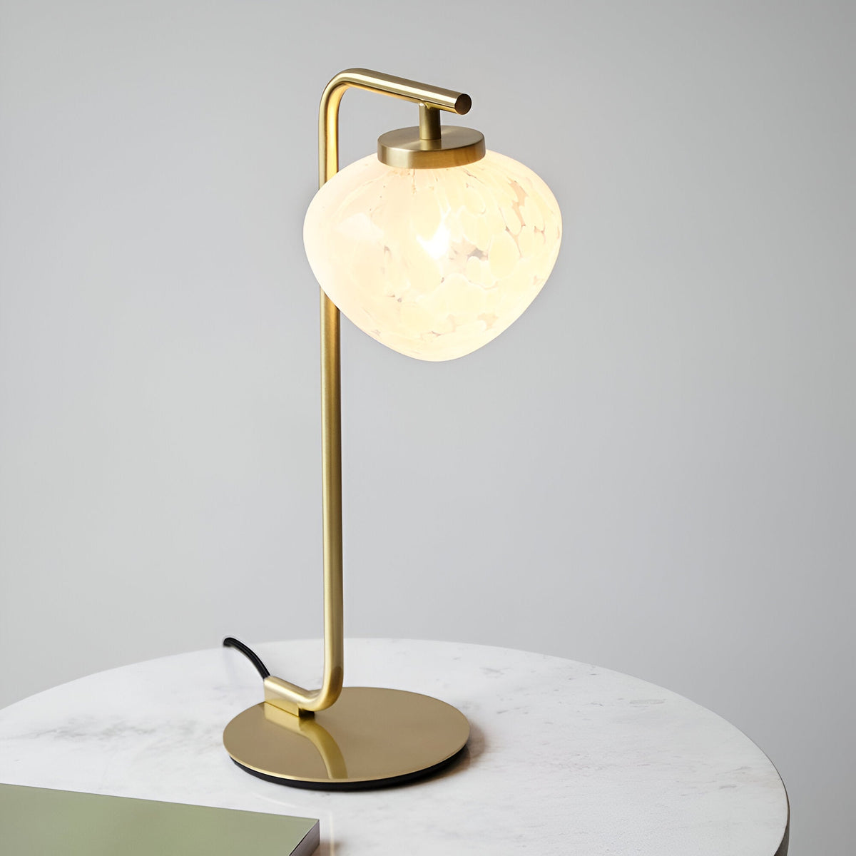 Endon Calloway satin brass table lamp with slim arched stem and white confetti blown glass shade, shown on a round marble side table.