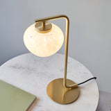 Endon Calloway table lamp in satin brass with a white confetti blown glass shade, shown on a round marble side table beside a green book.