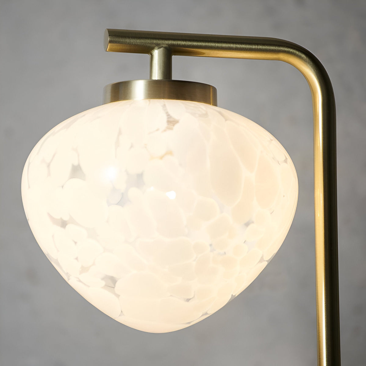 Close-up of the Endon Calloway table lamp shade in white confetti blown glass, suspended from a satin brass arm against a grey background.