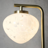 Close-up of the Endon Calloway table lamp shade in white confetti blown glass, suspended from a satin brass arm against a grey background.