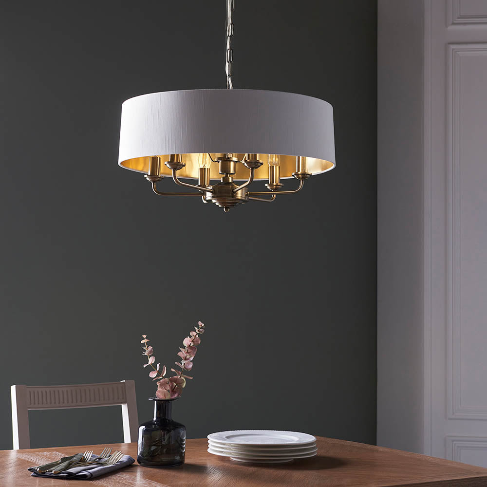 Endon Brenley V1 six-light pendant with a white drum shade, gold-lined interior and brass multi-arm fitting, hung above a wooden dining table.