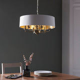 Endon Brenley V1 six-light pendant with a white drum shade, gold-lined interior and brass multi-arm fitting, hung above a wooden dining table.