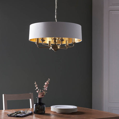 Endon Brenley V1 six-light pendant with a white drum shade, gold-lined interior and brass multi-arm fitting, hung above a wooden dining table.