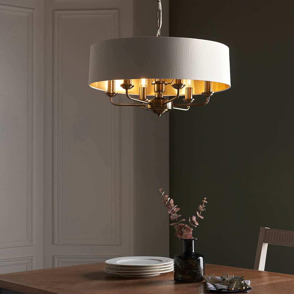 Endon Brenley V1 six-light pendant with white drum shade, gold-lined interior and antique brass multi-arm frame, suspended above a dining table.