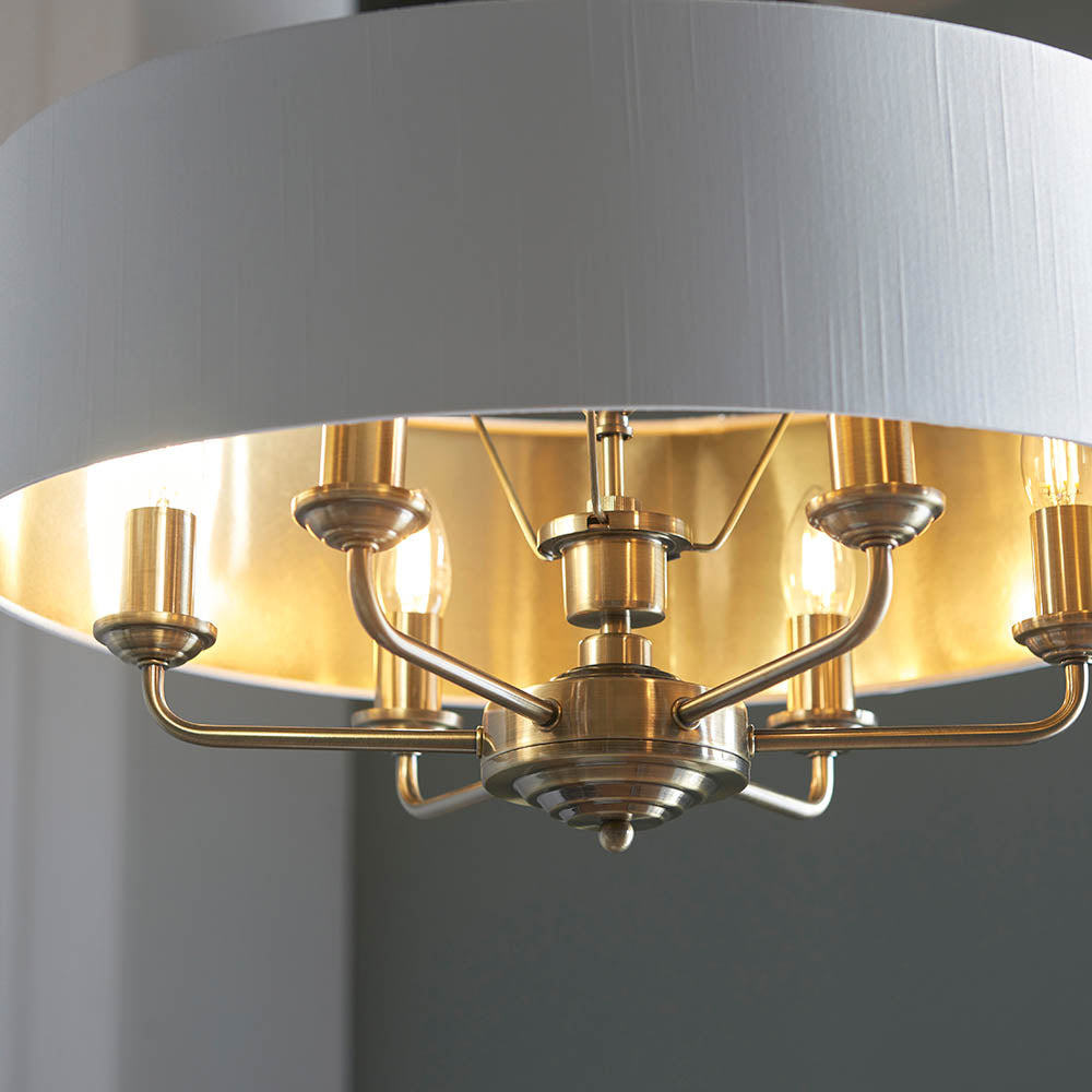 Close-up of Endon Brenley V1 6 light pendant showing antique brass arms holding six E14 lamps beneath a white fabric shade with gold-lined interior.