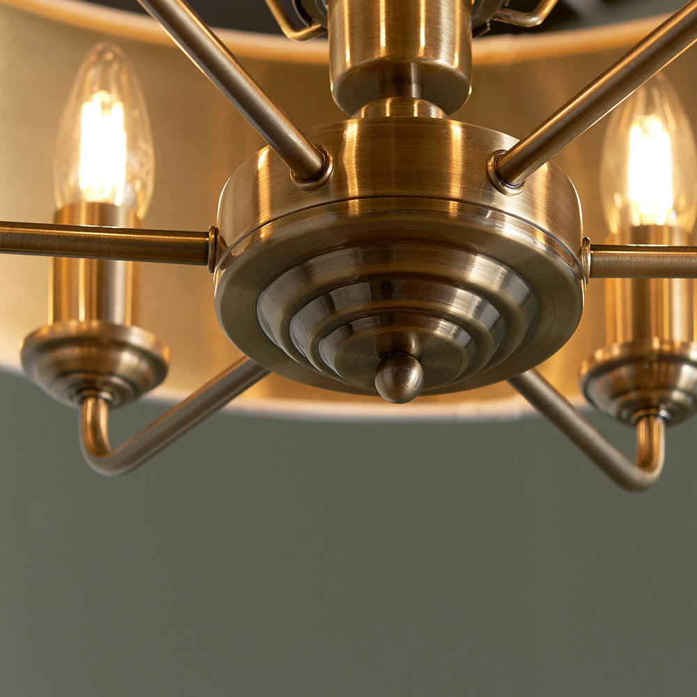 Endon Brenley 6 light pendant close-up with antique brass tiered hub, radiating arms, and lit candle bulbs against a gold-lined shade.
