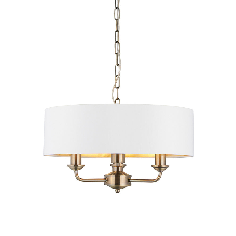 Endon Brenley 3 light pendant in antique brass with a vintage white drum shade and gold-lined interior, suspended on a chain against a white background.