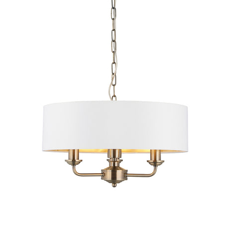 Endon Brenley 3 light pendant in antique brass with a vintage white drum shade and gold-lined interior, suspended on a chain against a white background.