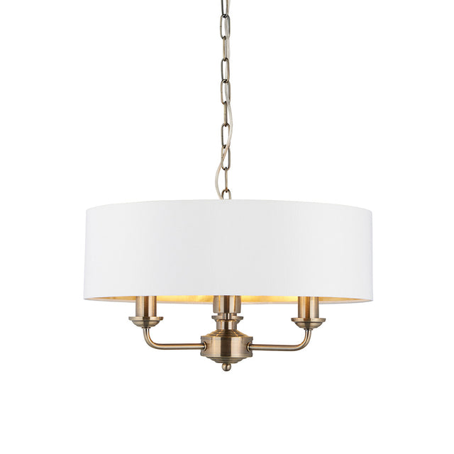 Endon Brenley 3 light pendant in antique brass with a vintage white drum shade and gold-lined interior, suspended on a chain against a white background.