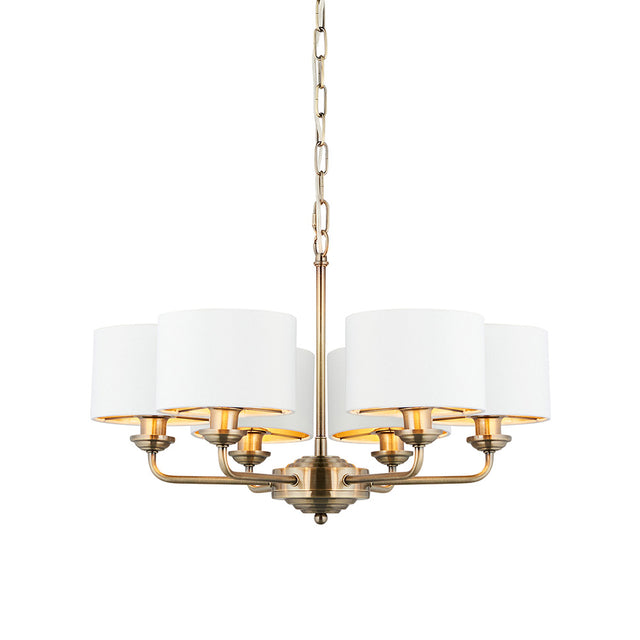Brenley V2 six-light pendant with antique brass metalwork, six white fabric drum shades, and a chain suspension, shown on a plain white background.