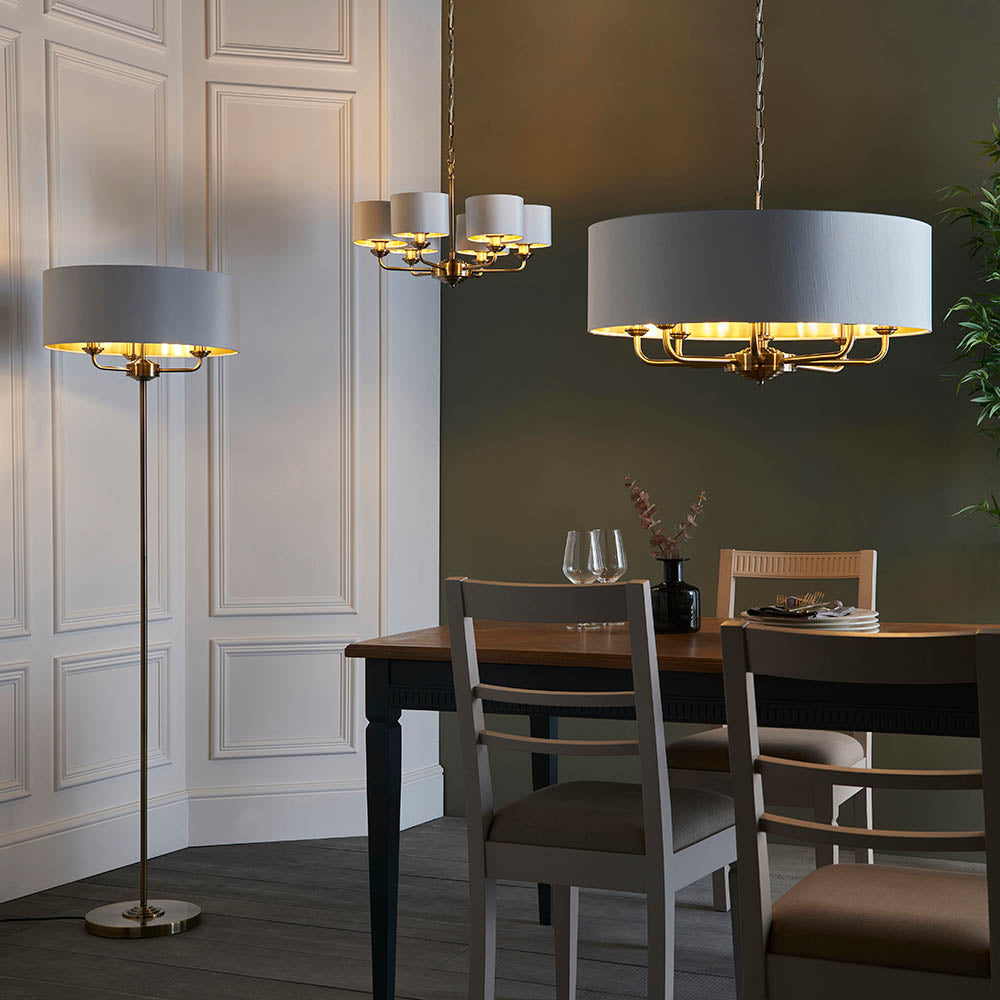Brenley V2 6 Light Pendant in white with gold-toned metal arms, shown above a dining table alongside a matching floor lamp and chandelier.