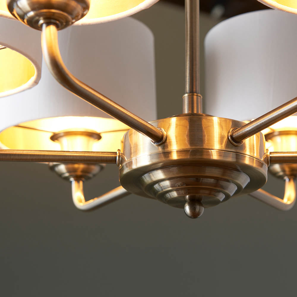 Close-up of the Brenley V2 6 light pendant's antique brass centre hub with curved arms and white fabric shades against a neutral background.