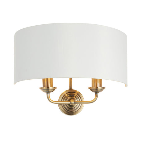 Endon Brenley 2 light wall light with a curved white linen half-shade on an antique brass twin-arm backplate, shown on a plain white background.