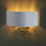 Endon Brenley 2 light wall light with a curved white linen shade on an antique brass backplate, casting a warm upward glow against a neutral wall.