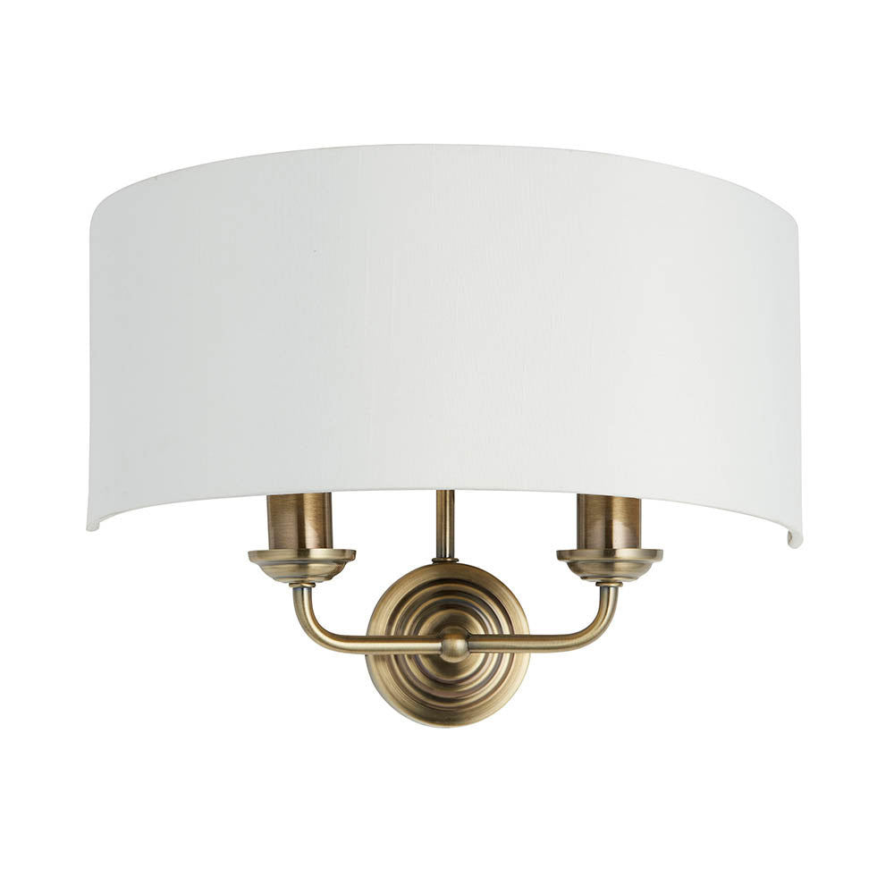Endon Brenley 2 light wall light with antique brass twin arms, curved white linen half-shade and round backplate, shown on a plain white background.