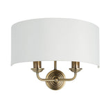 Endon Brenley 2 light wall light with antique brass twin arms, curved white linen half-shade and round backplate, shown on a plain white background.