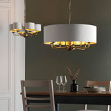 Endon Brenley 8 light pendant in brass with white drum shade and gold-lined interior, shown beside a smaller matching chandelier above a dining table.