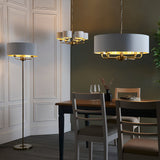 Endon Brenley pendant with white drum shade and brass arms shown above a dining table alongside matching chandelier and floor lamp in a panelled room.