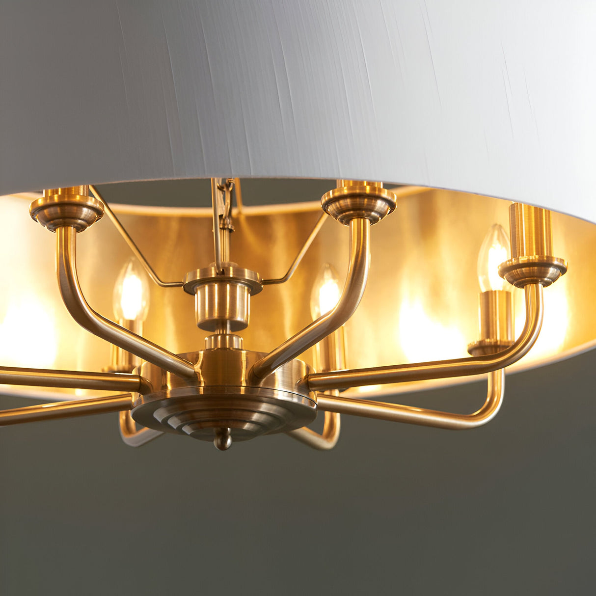 Close-up of Endon Brenley 8 light pendant showing antique brass arms, candle lamps and gold-lined vintage white fabric shade interior.