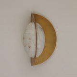 Althia LED Alabaster Wall Light in brushed brass, with a rounded natural alabaster diffuser set against a half-moon brass backplate, shown on a plain light background.