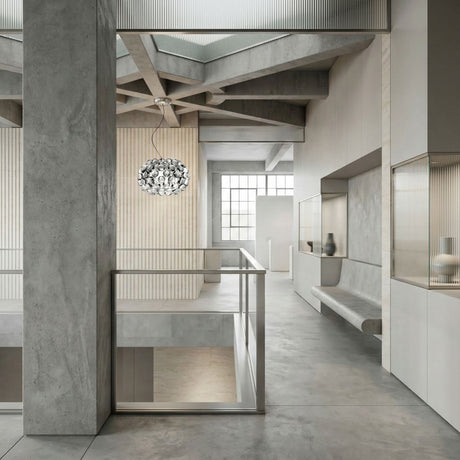 A modern, minimalist interior with concrete walls and floors, large windows, geometric ceiling beams, built-in seating, neutral tones, and a Briller LED Small Pendant Light in transparent as a centerpiece.