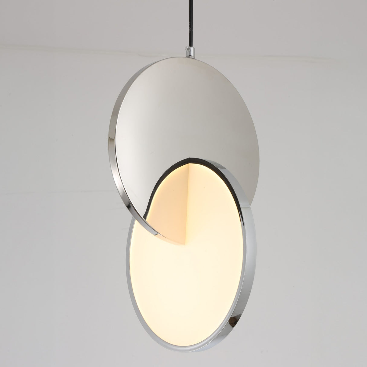 The Half Moon LED Pendant Light - Silver features two overlapping circular metallic discs—one LED-lit, one reflective—suspended from a thin black cord, creating a modern look against a white background.