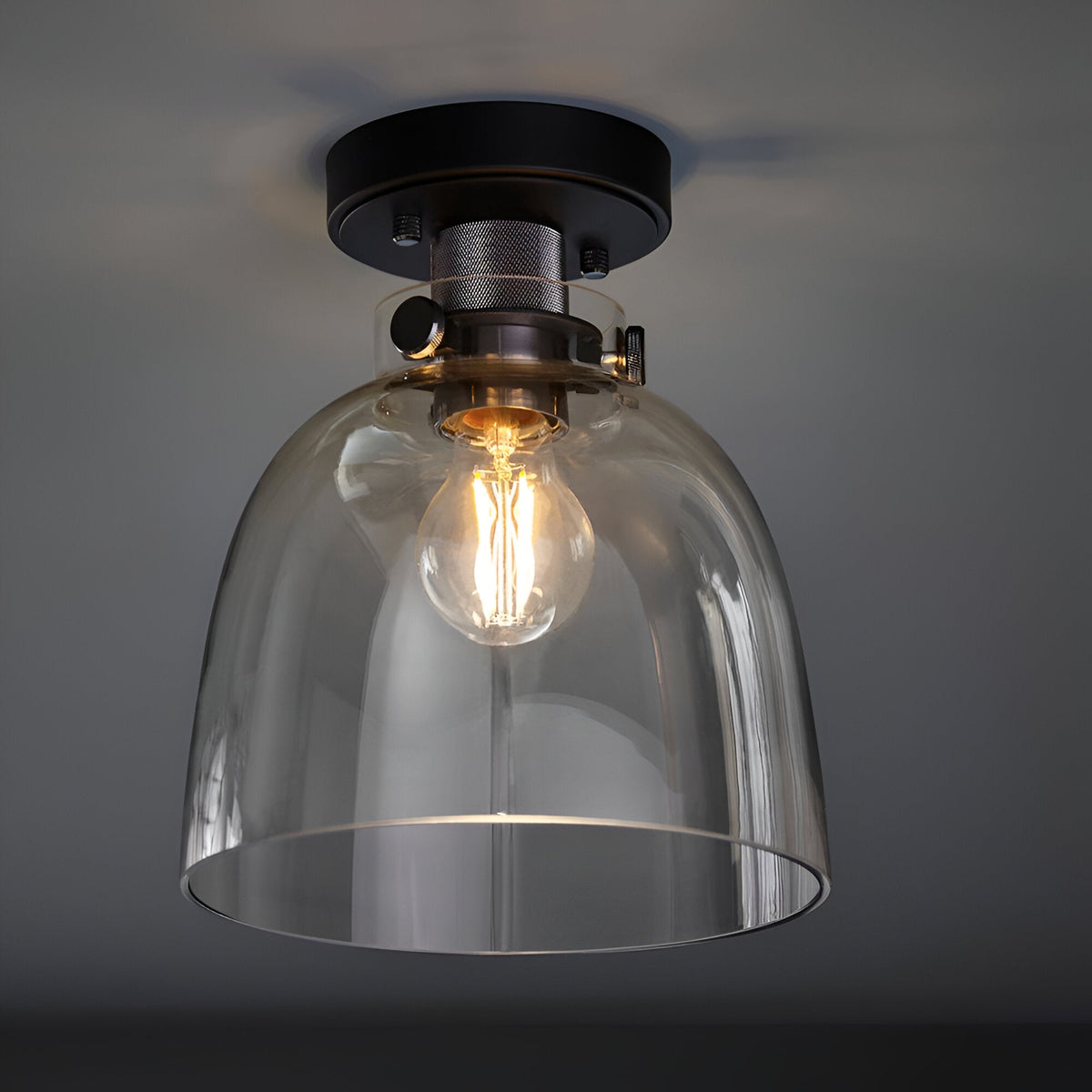 Endon Camden matt black flush ceiling light with a clear glass dome shade and single E27 filament bulb, mounted to a grey ceiling.