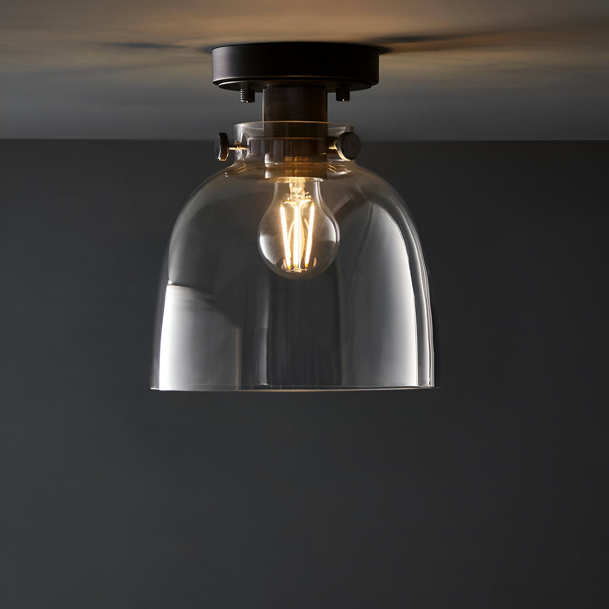 Endon Camden flush ceiling light in matt black with a compact clear glass dome shade and single E27 filament bulb, mounted to a grey ceiling.