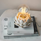 Aldgrove Table Lamp with oatmeal crackle glaze ceramic artichoke-shaped base and antique brass neck detail, lit E27 bulb, shown on stacked books.