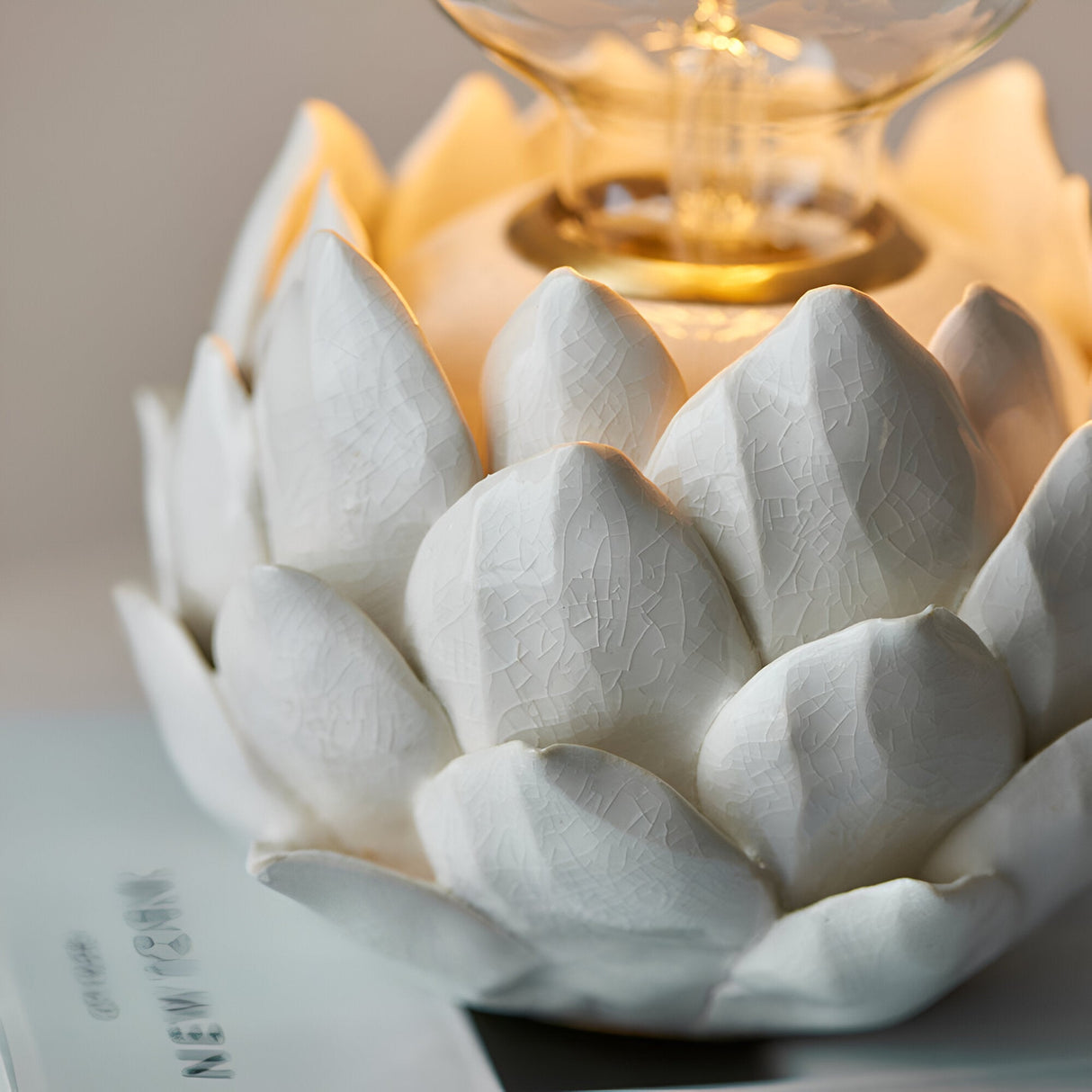 Aldgrove Table Lamp in Antique Brass, close-up of the artichoke-shaped ceramic base with oatmeal crackle glaze and lit E27 bulb detail.