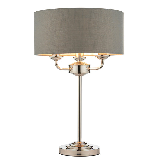 Endon Brenley 3 light table lamp with grey linen drum shade, nickel three-arm fitting and slim stem on a round base, shown on a white background.