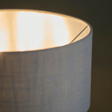 Close-up of the Endon Brenley 3 Light Table Lamp showing its grey linen-mix drum shade illuminated with a brushed metallic reflective inner lining.