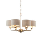 Brenley 6-light pendant with brass fittings and six curved arms holding natural linen drum shades, suspended from a chain, on a plain white background.