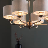 Brenley six-light pendant with brass and chrome finish, multiple arms holding fabric drum shades, shown lit in a dark-walled room.