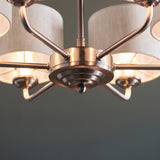 Close-up of the Brenley 6 light pendant's brushed chrome centre hub with tiered detailing and six angled arms holding natural linen shades.