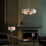 Brenley 6 Light Pendant in brass and chrome with fabric drum shades, shown above a fireplace in a living room, paired with a matching table lamp.
