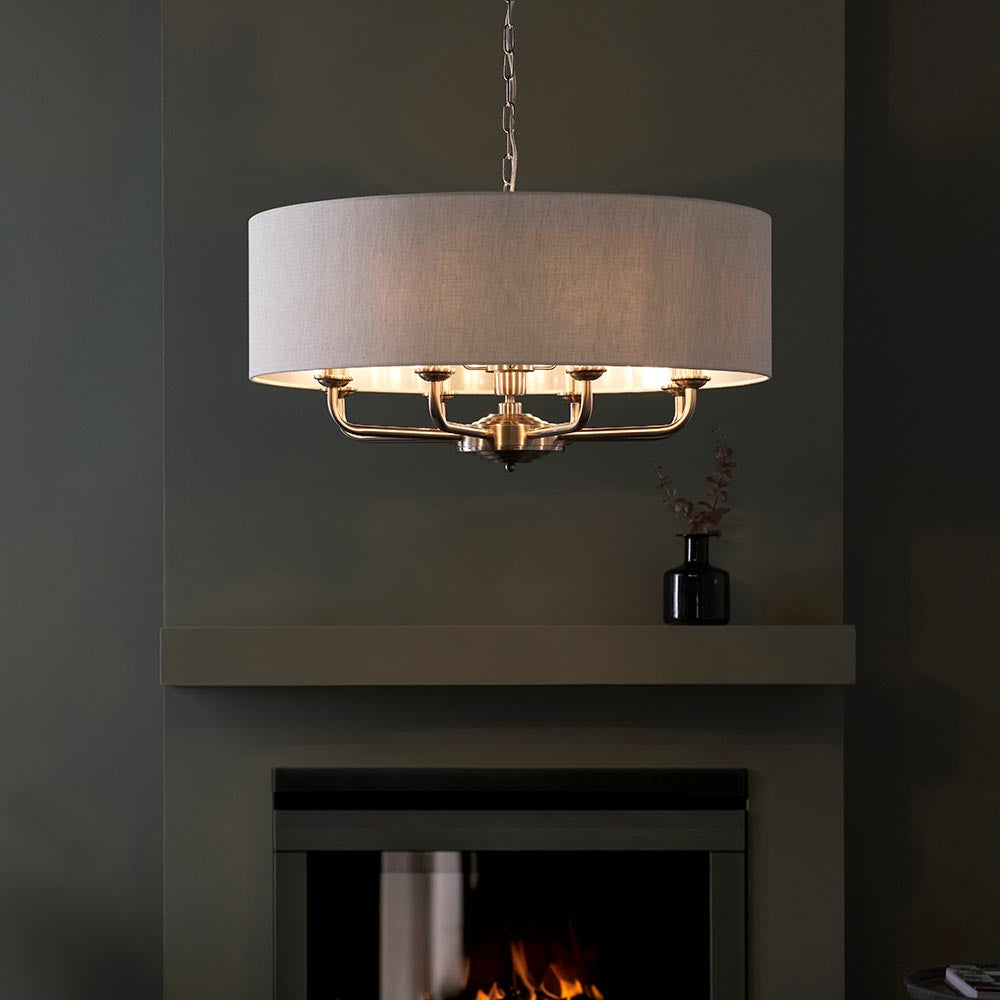 Endon Brenley 8 light pendant in chrome and brass with natural linen drum shade, hanging from a chain above a fireplace in a dark grey room.