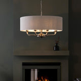 Endon Brenley 8 light pendant in chrome and brass with natural linen drum shade, hanging from a chain above a fireplace in a dark grey room.