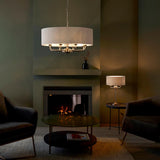 Endon Brenley pendant light with natural linen drum shade and chrome multi-arm fitting, above a fireplace in a green-walled living room.