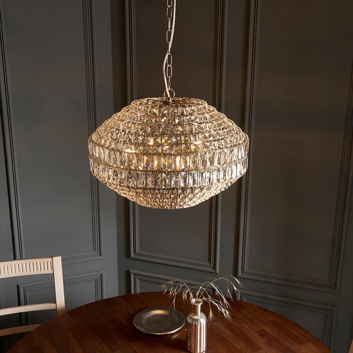 Endon Aldton 5 light pendant with rounded tiered crystal shade on polished nickel chain, hung above a wooden dining table against grey panelled walls.